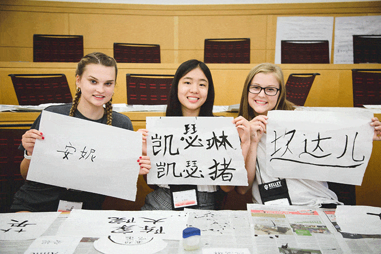 Three girls holding up paper with Mandarin writing.